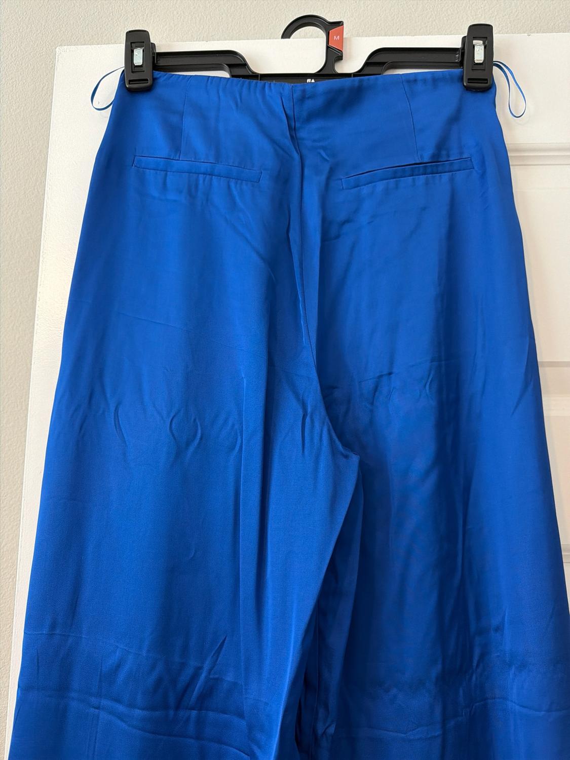 Blue trousers hanging from a black hanger on a white door. Two back pockets and a label with the text M are visible.