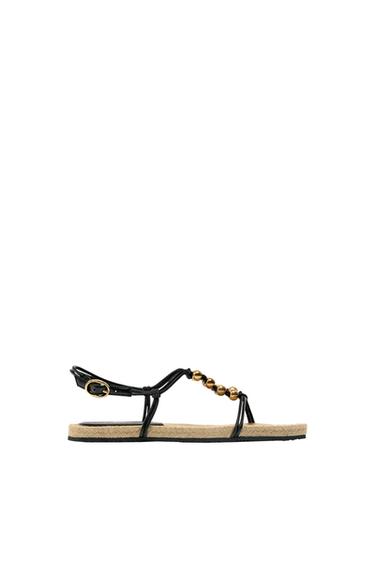 Side view of a black sandal with gold beads and a jute sole.