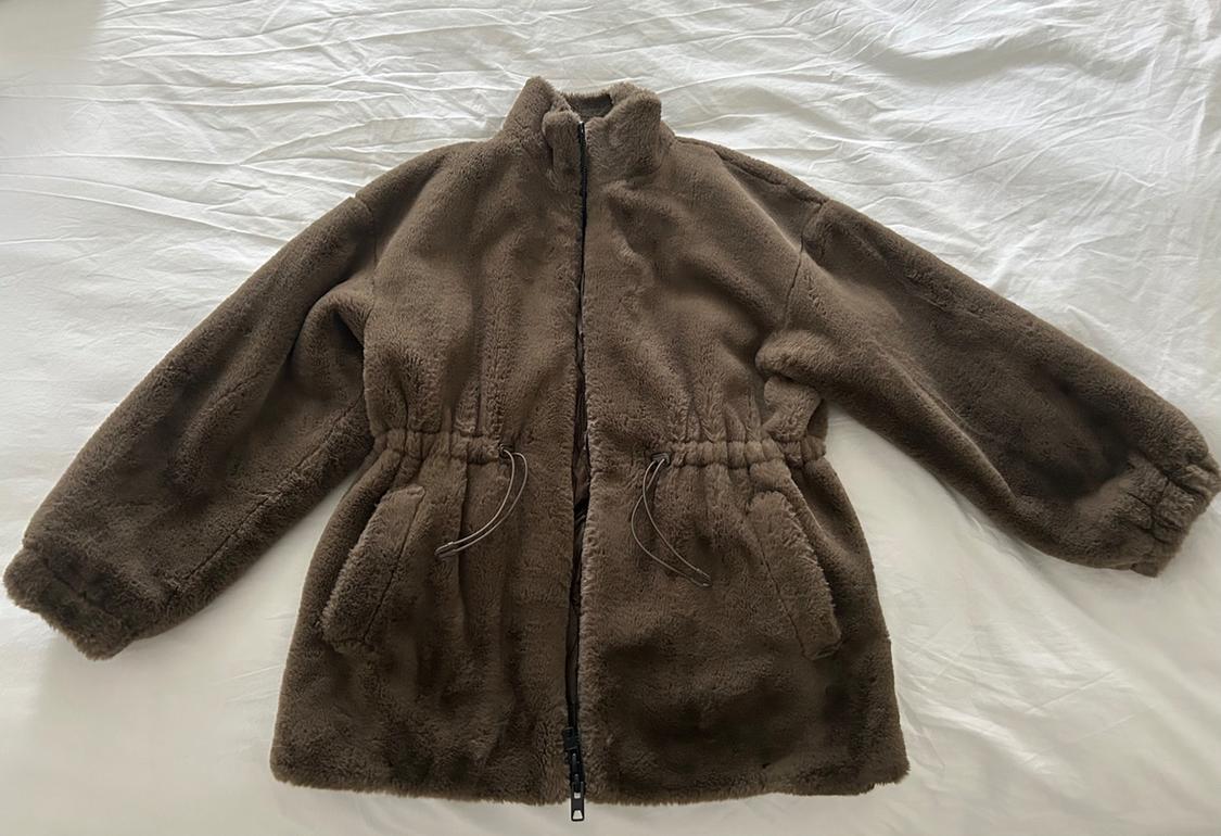 Brown fleece jacket with a front zip and drawstrings at the waist, on a crumpled white surface.