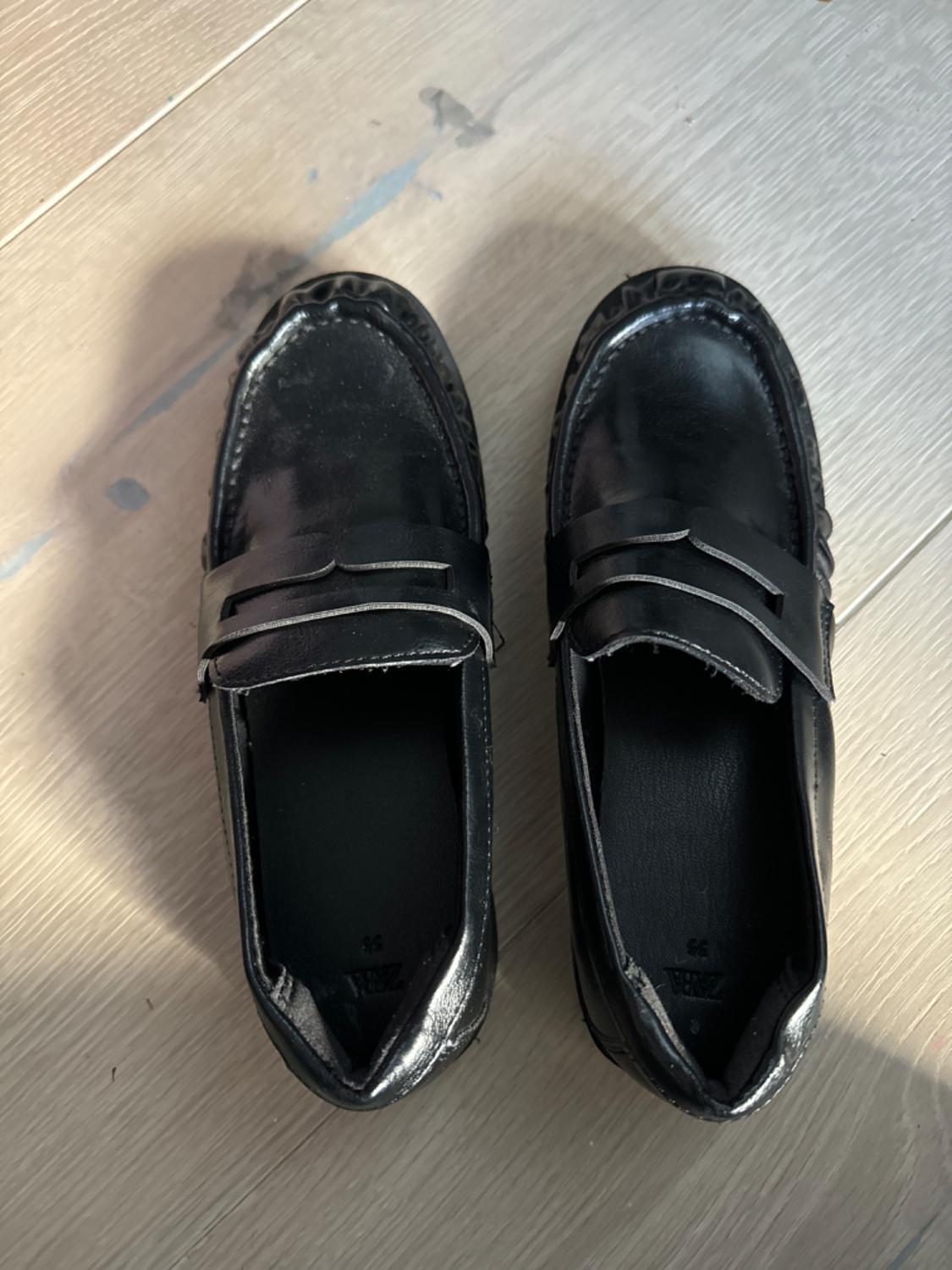 Black patent leather shoes with a classic design, viewed from above on a light wooden floor.