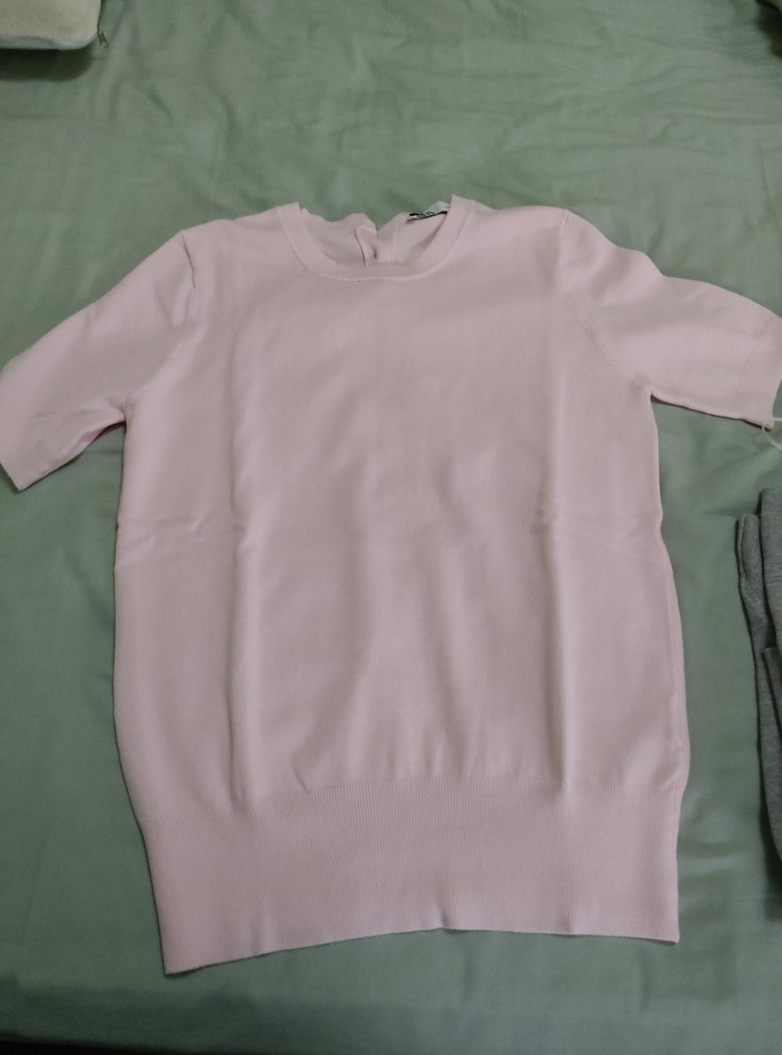 Light pink short-sleeved knitted top with a round neck and ribbed hem, laid on a light green sheet in a casual composition.