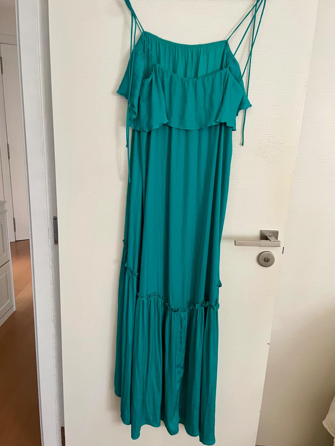 Long green dress with thin straps, featuring ruffles on the neckline and skirt, hanging on a white interior door, relaxed style.