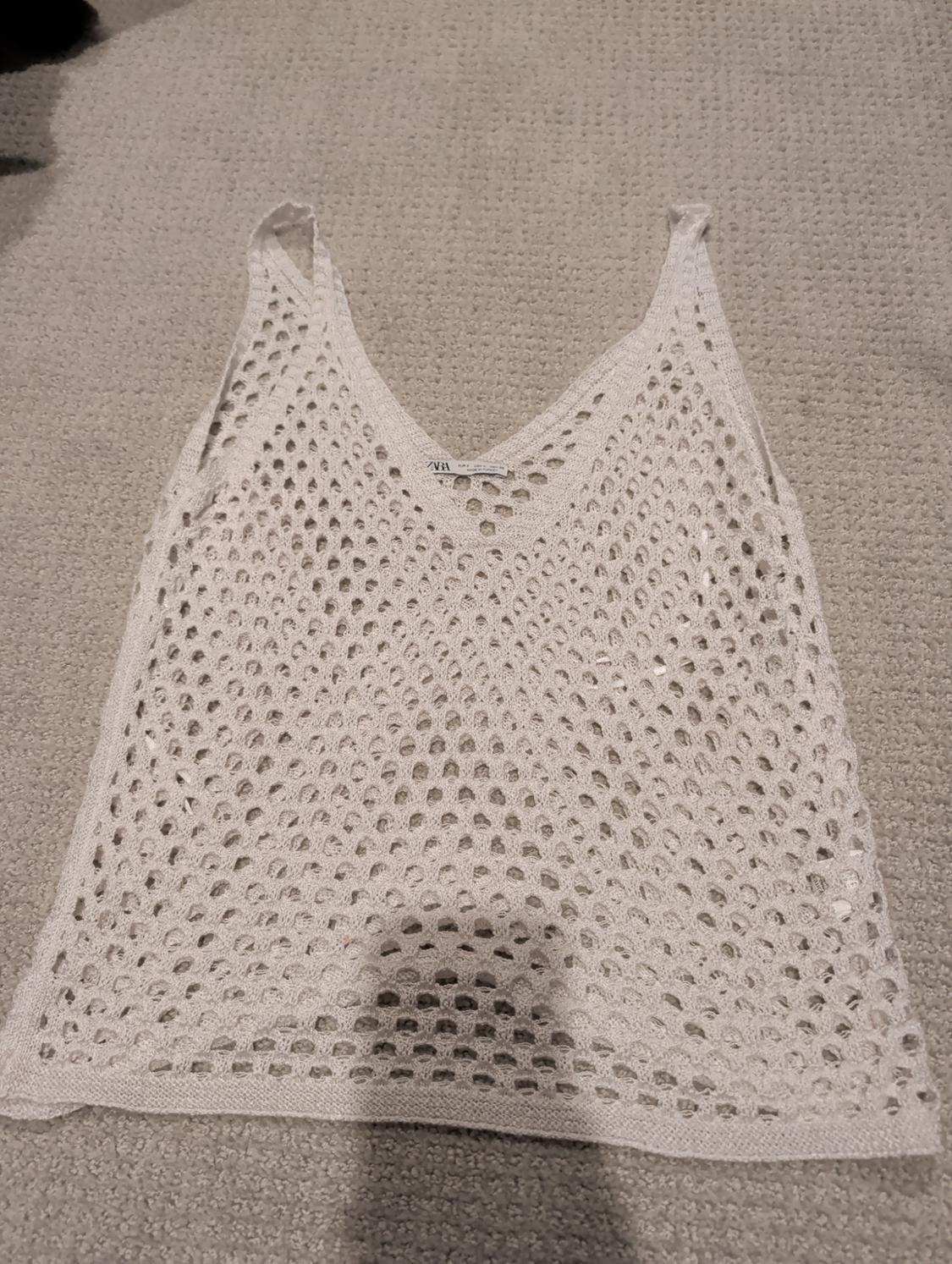White open-knit top on a beige rug, with a visible label in the centre of the V-neckline.