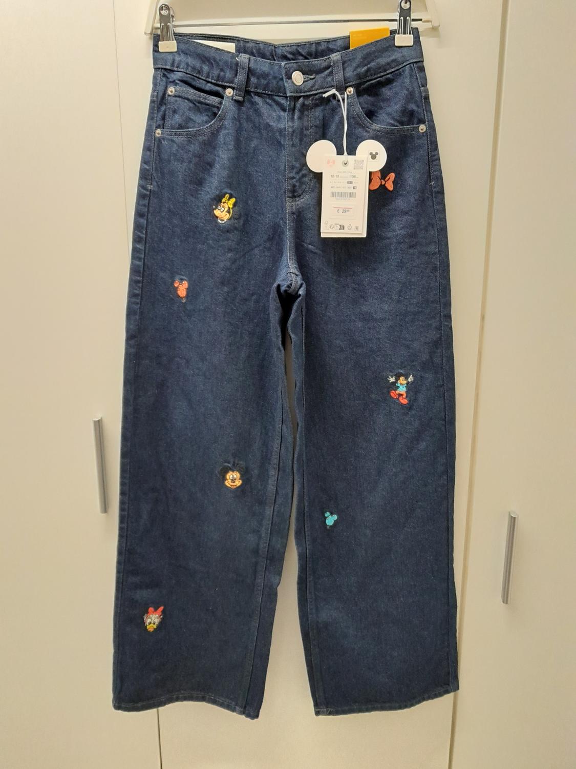 Blue denim jeans with embroidered cartoon characters and a mouse-head shaped hang tag.