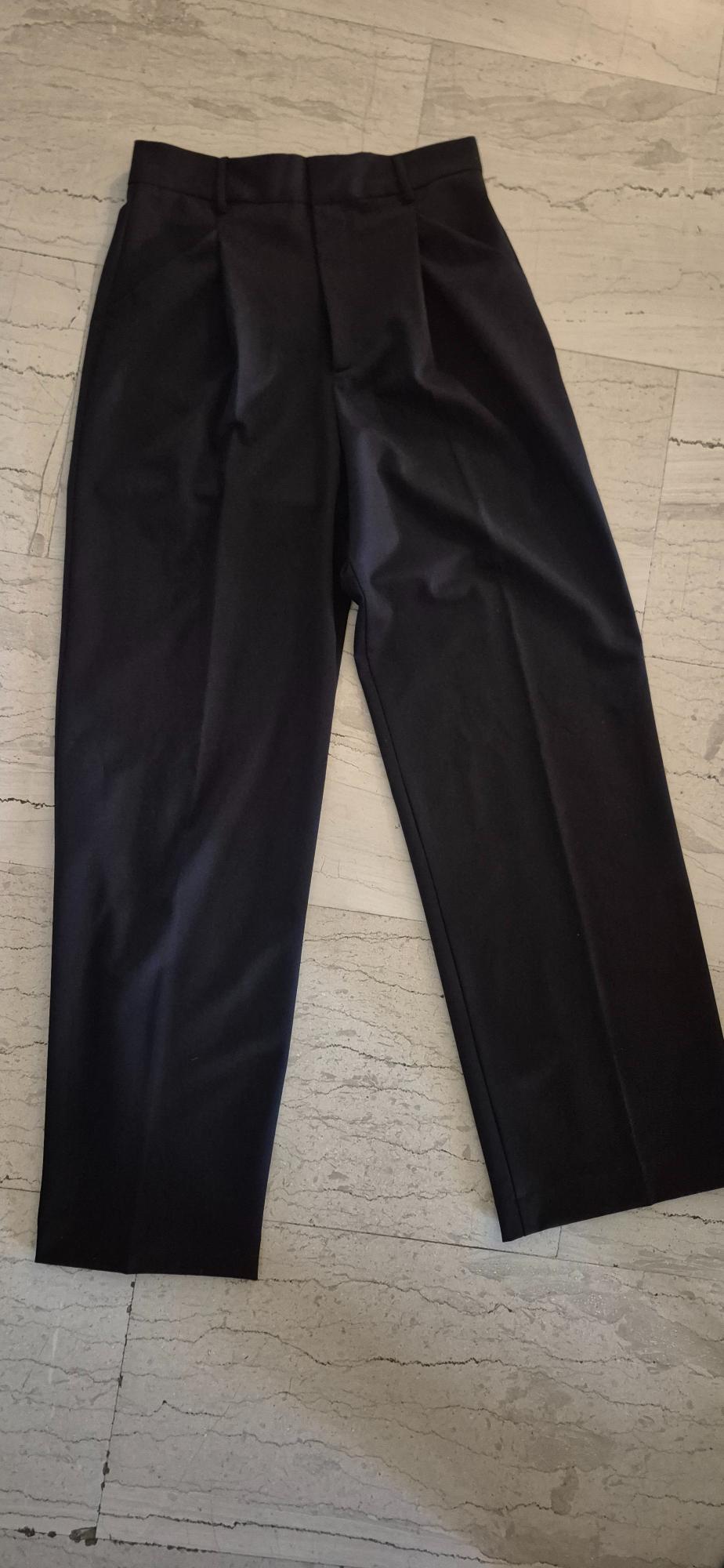 Black dress trousers on a light marble floor, showing creases and a classic design with pockets and belt loops.