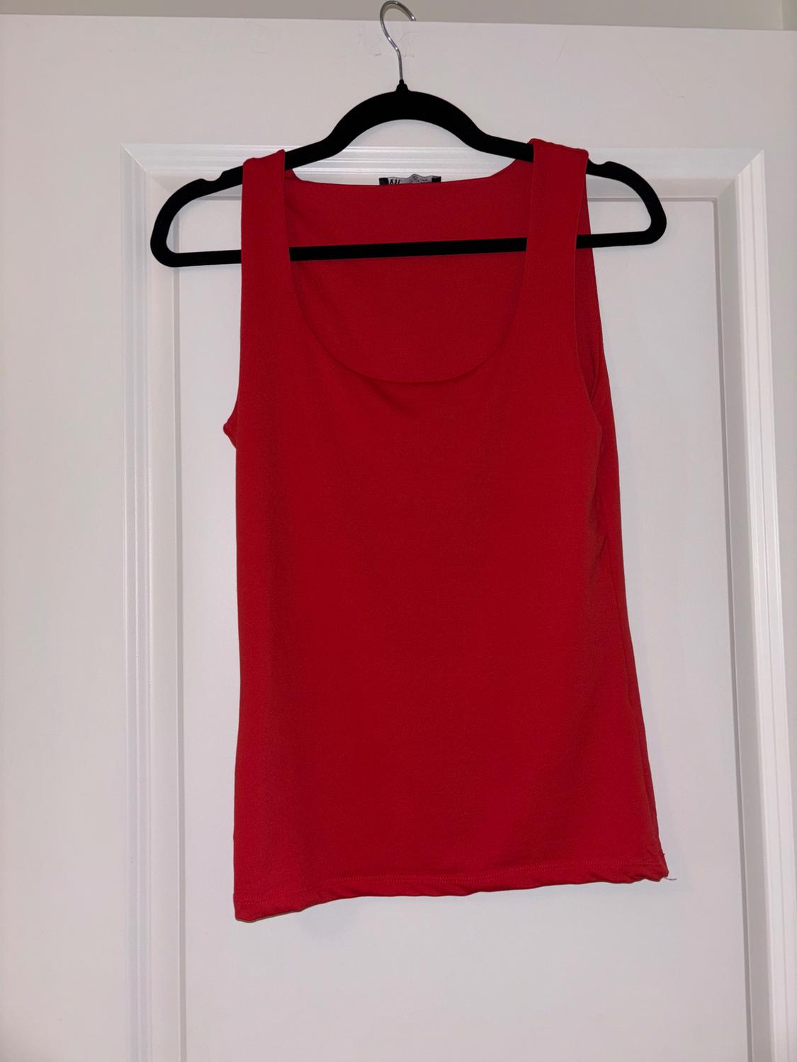 Red sleeveless top hanging on a black coat hanger over a white door.