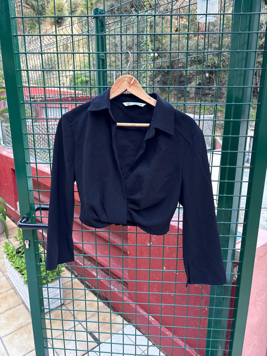 Black long-sleeved shirt hanging on a wooden hanger over a green mesh door, with a garden background and red wall.