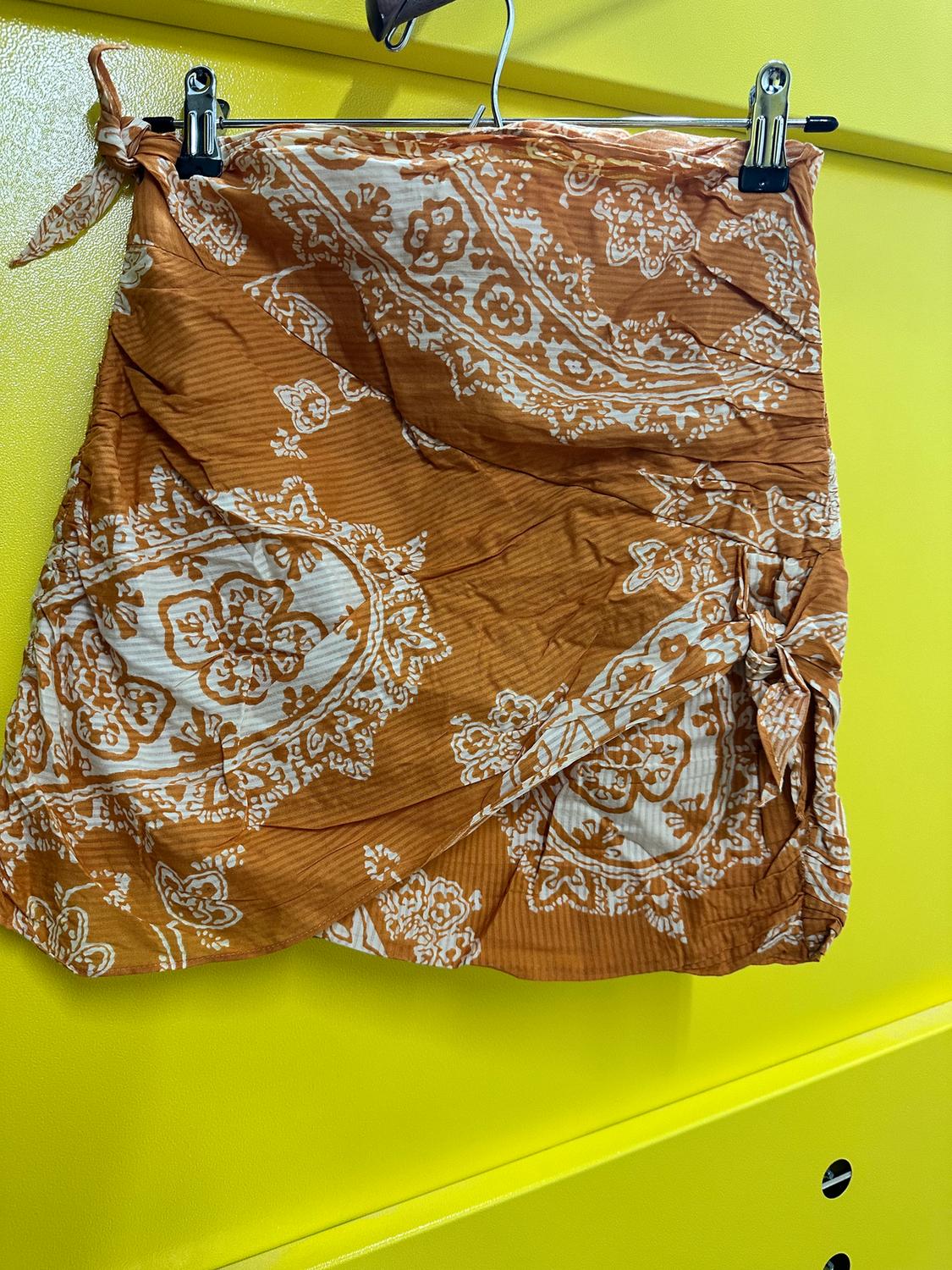 Brown skirt with a white pattern hanging on a hanger against a bright yellow background.