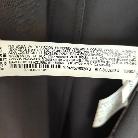 Clothing label with Inditex manufacturing and distribution information, including addresses and barcodes, on dark fabric.