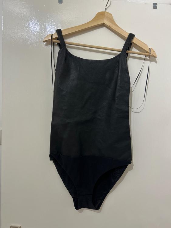 Black strappy bodysuit hanging on a wooden hanger over a white door.
