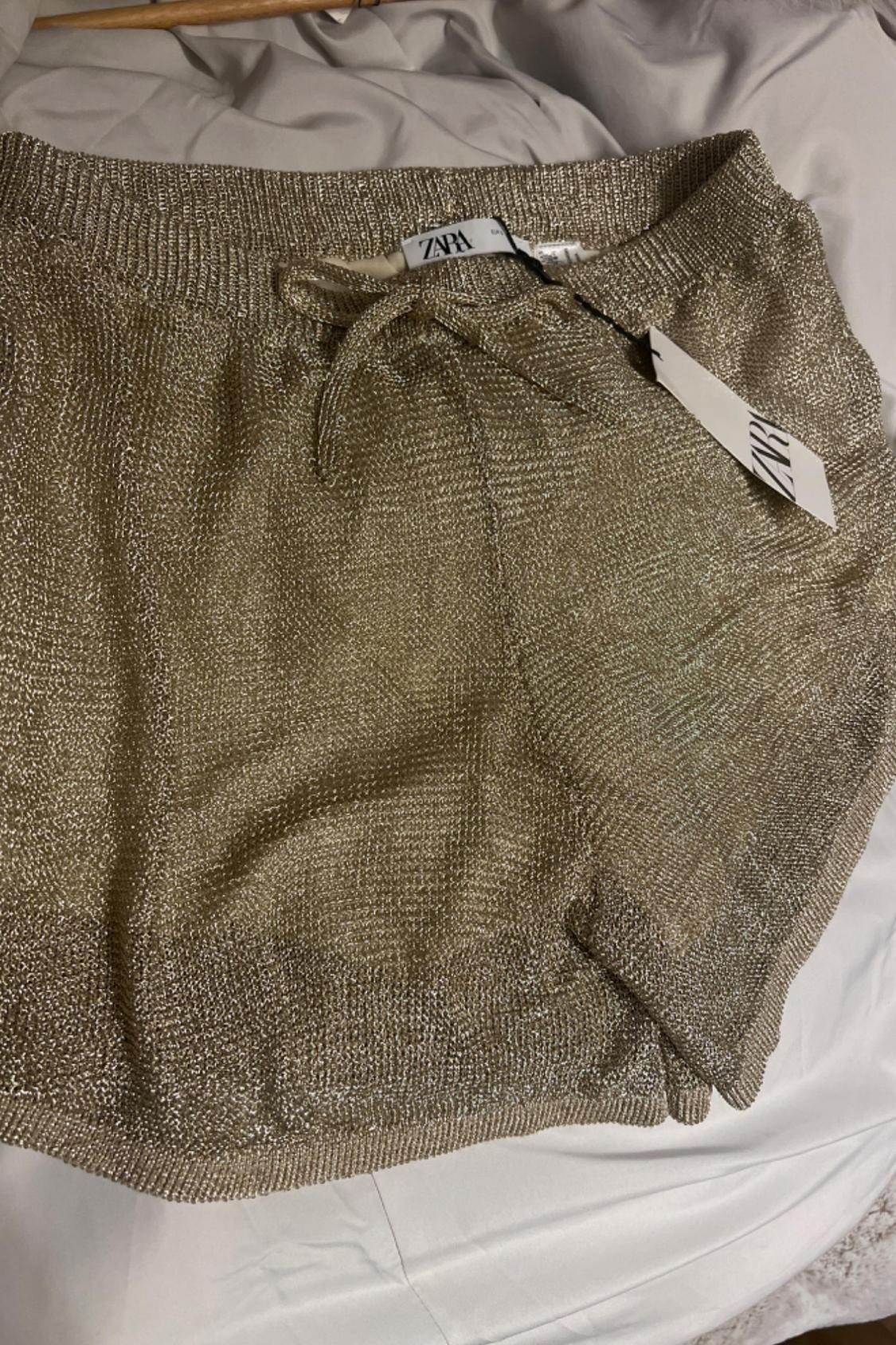 Detail of gold shorts with visible ZARA label.