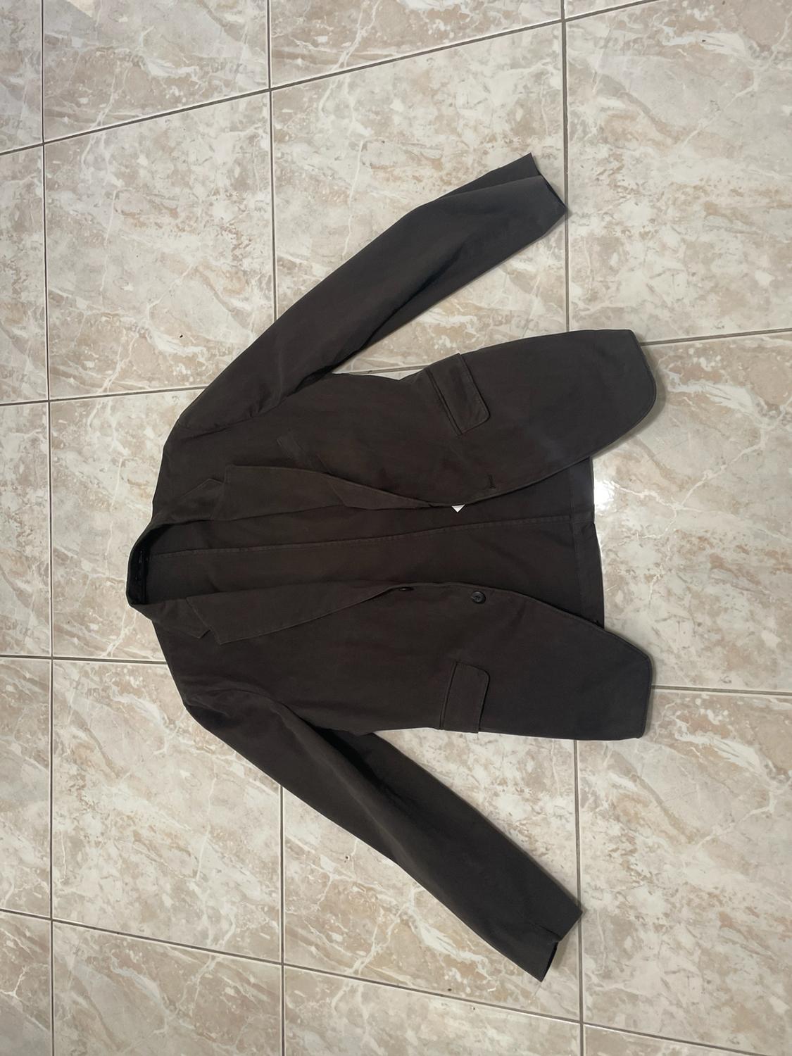 Dark blazer with lapels and pockets, laid flat on a light-tiled floor.