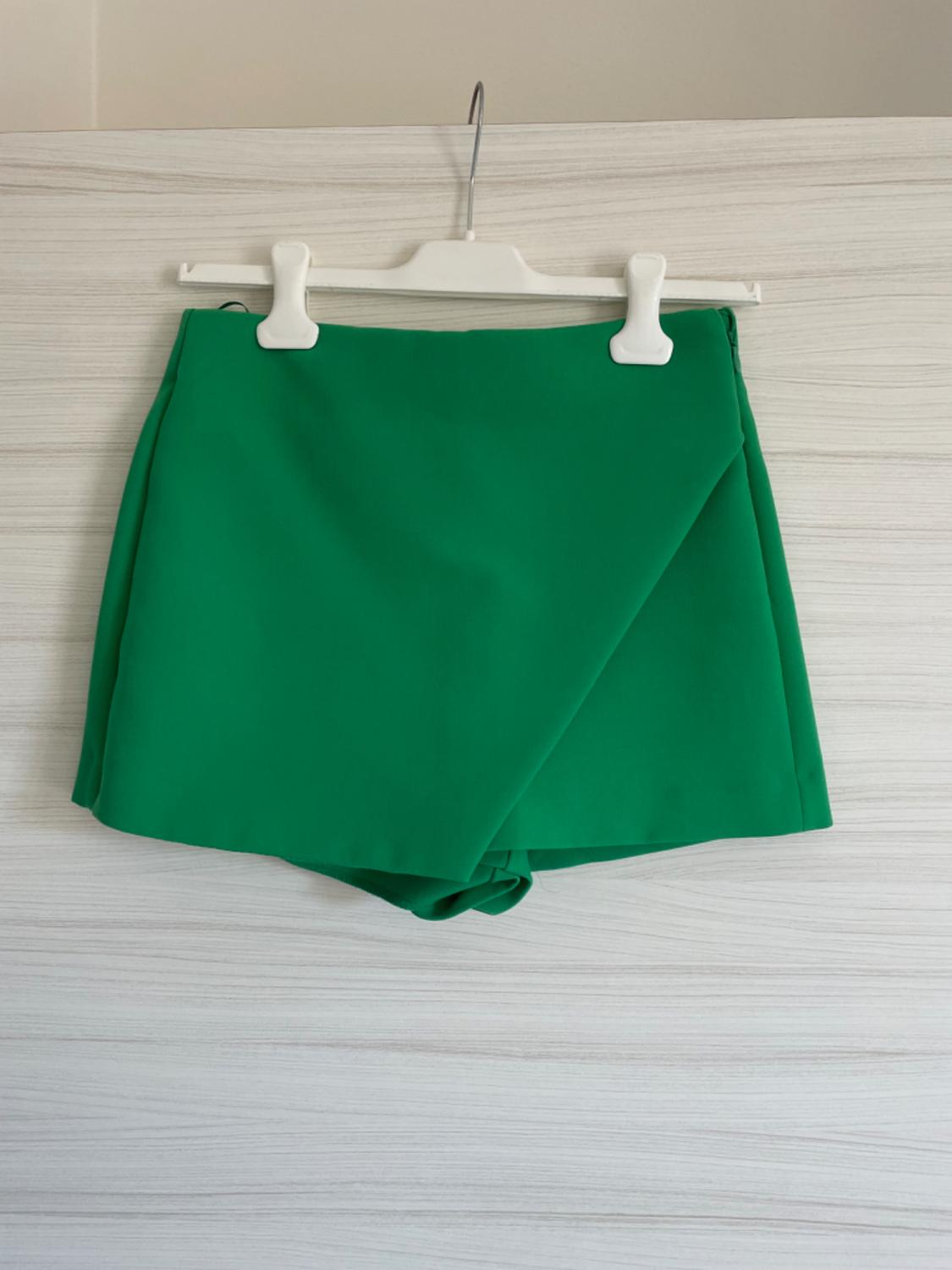 Green mini skirt hanging on a white hanger against a light wooden background.