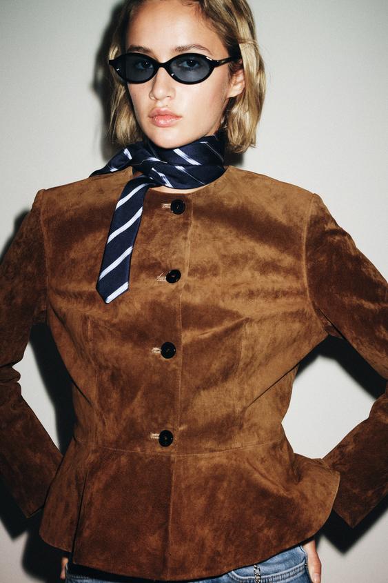 Střední záběr bundy barvy whiskey s kulatým výstřihem, dlouhými rukávy a předním zapínáním na knoflíky.