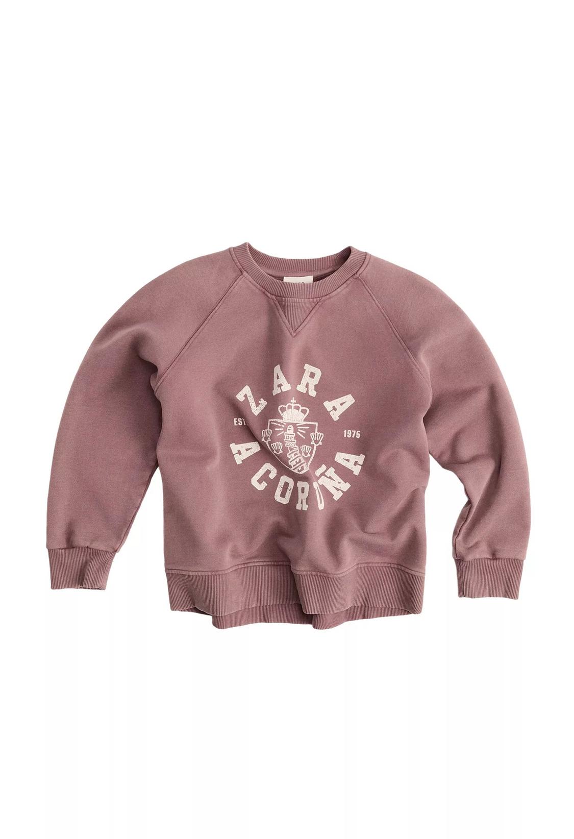 Pink sweatshirt with the text ZARA A CORUÑA EST 1975 and a crest in the center, against a white background.