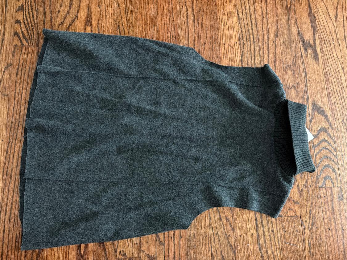Top in gray knit with a high neck, laid out over a wooden floor.