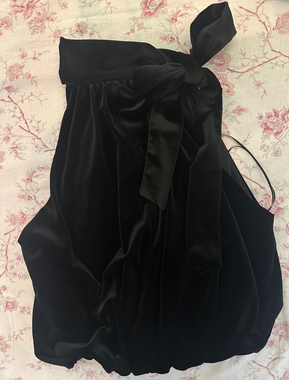 Black velvet dress with a large bow, on a white fabric background with a pink floral print.