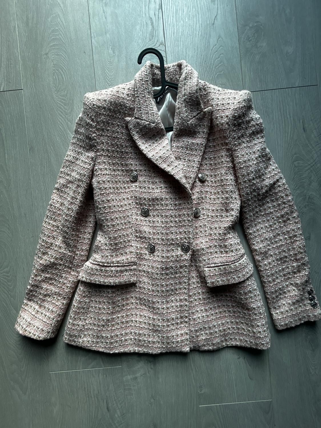 Pink and white marl texture double-breasted blazer, with metal buttons and flap pockets, on a hanger against a wooden floor.