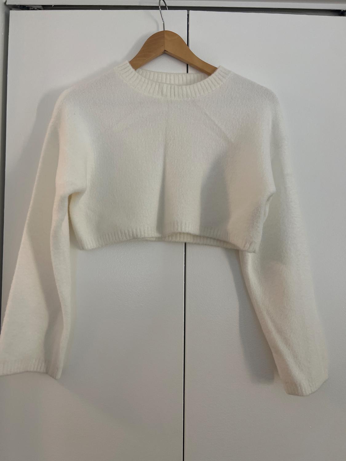 Front view of a white cropped sweater with long sleeves and a round neck.
