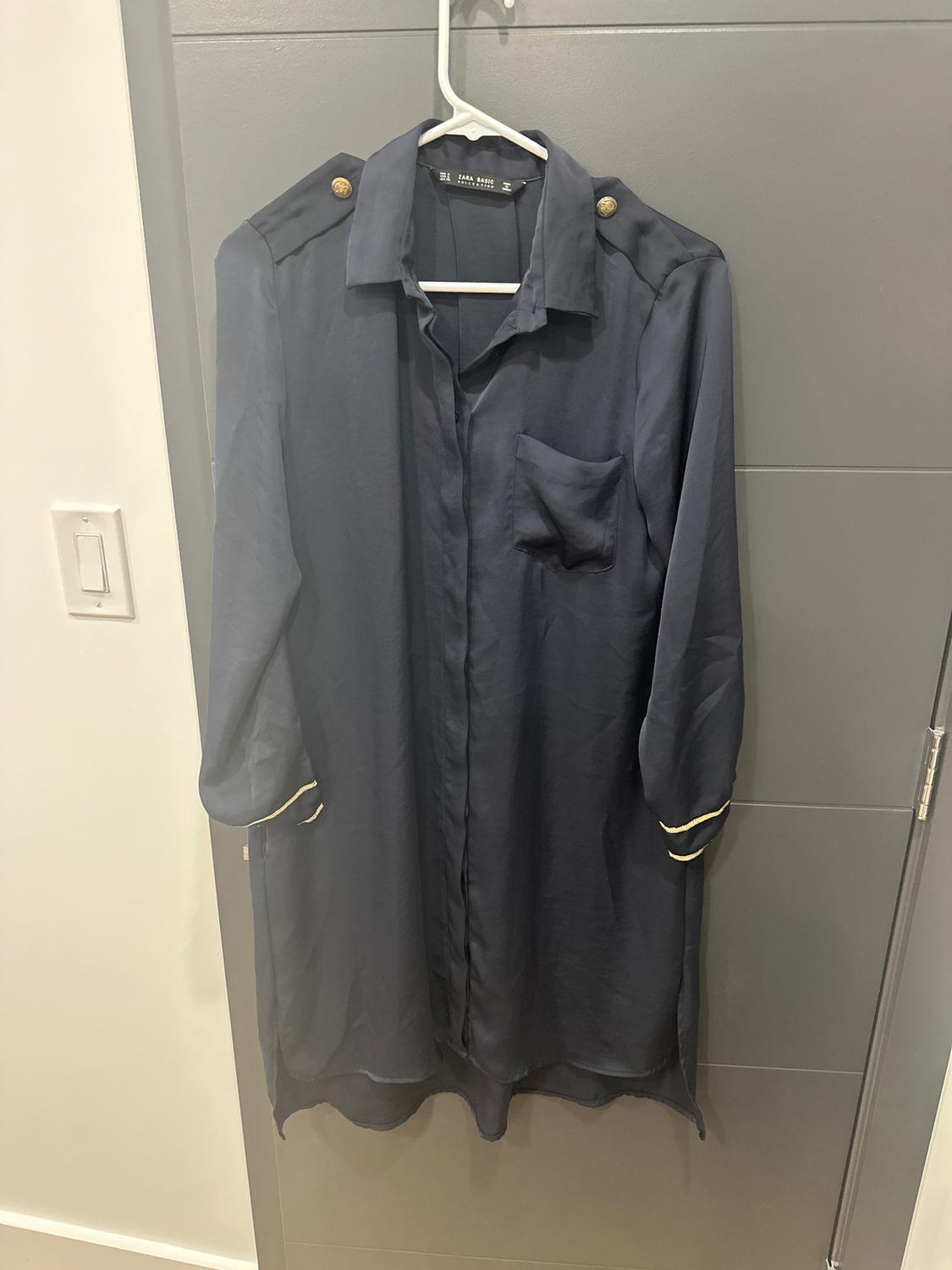 Dark blue dress hanging on a white hanger, with gold buttons on the shoulders and a chest pocket. Gray door in the background.