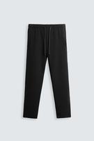 Front view of black trousers with adjustable elasticated waistband and drawstring. Front pockets and jetted pockets at the back.