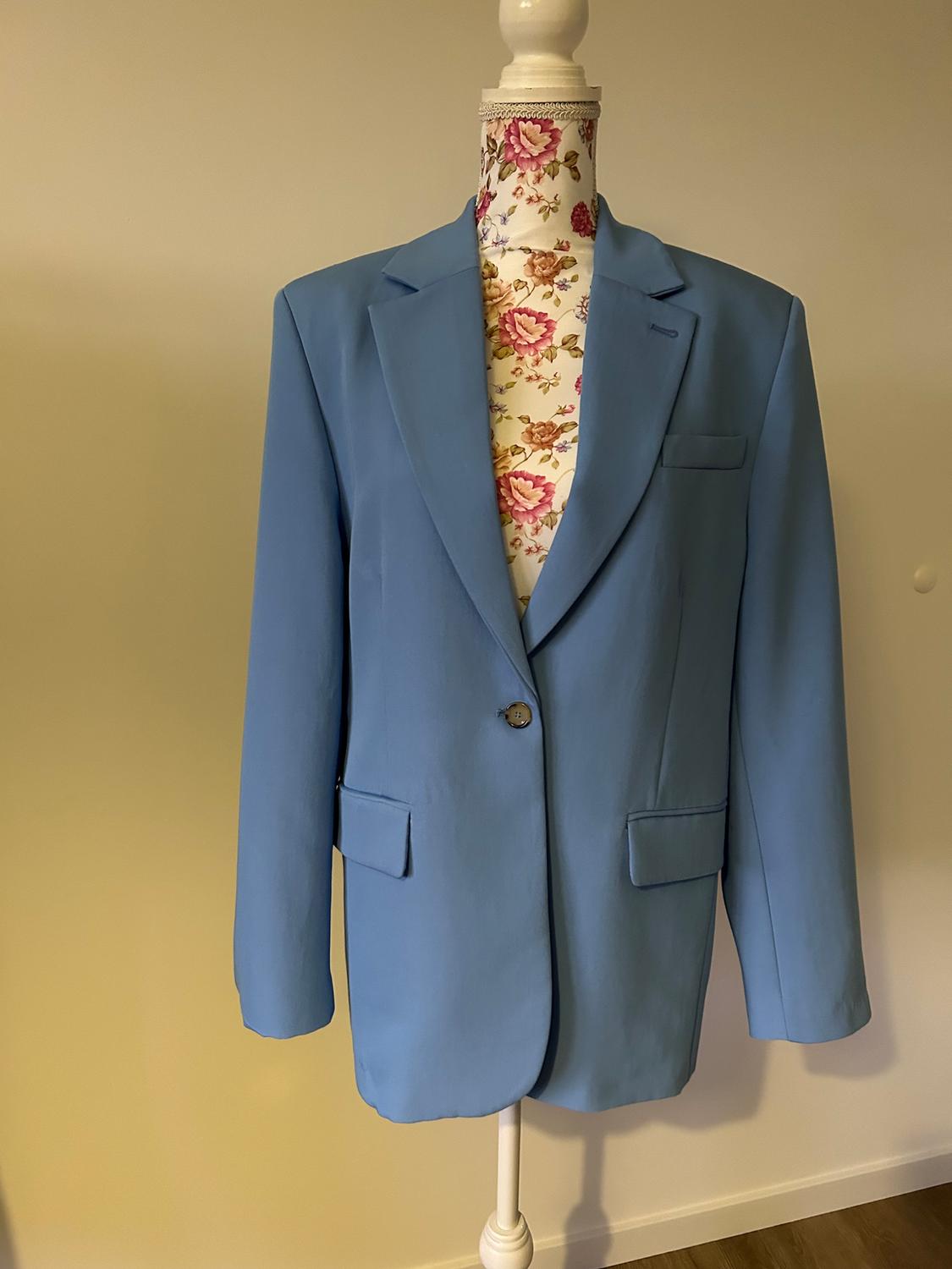 Mannequin in a light blue, single-button jacket, beige background. Mannequin in a floral print in pink and green tones.