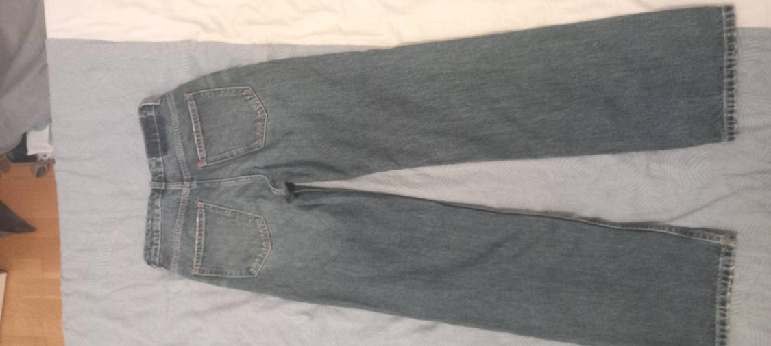 Blue wide-leg jeans viewed from behind, laid out on crumpled light-coloured sheets with a wooden floor to the side.