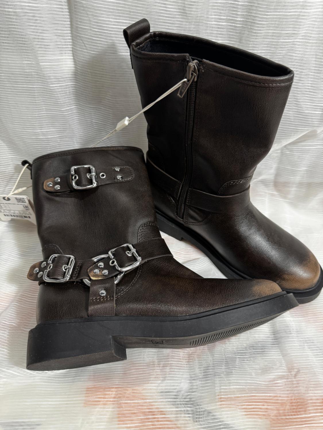 Side view of black boots with metal buckles and a side zip.