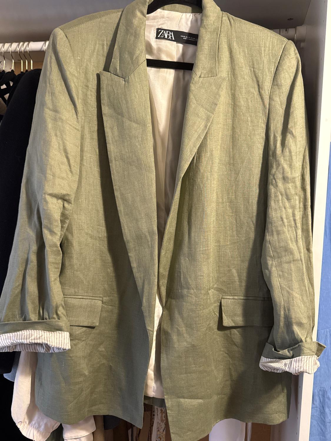 Olive green linen jacket hanging in a wardrobe, with rolled-up sleeves and a visible Zara label inside.