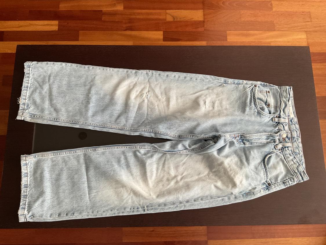 Light blue distressed denim jeans, placed on a dark wooden table in an indoor setting.