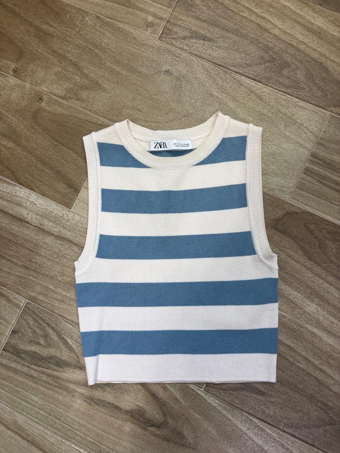 Blue and white striped sleeveless top on a wooden floor. Visible tag with text: "ZARA".