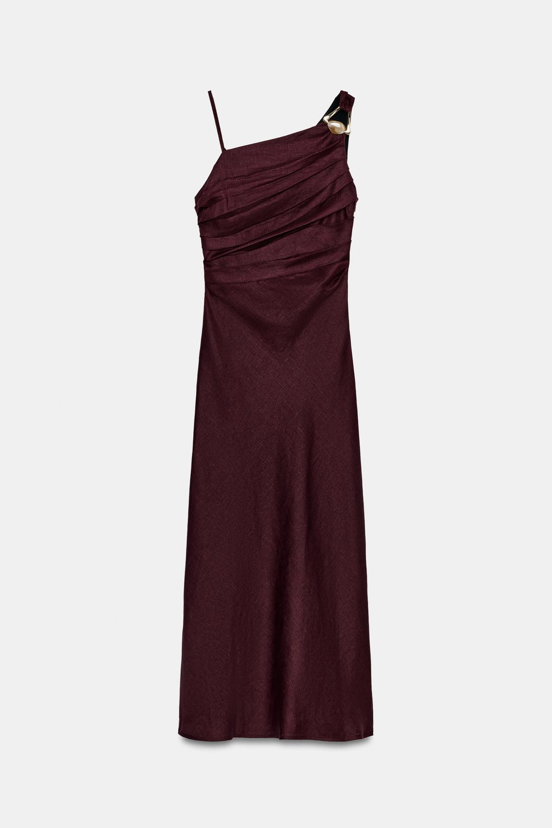 Front view of an aubergine midi dress with an asymmetric neckline and straps, a gold appliqué, and front pleats.