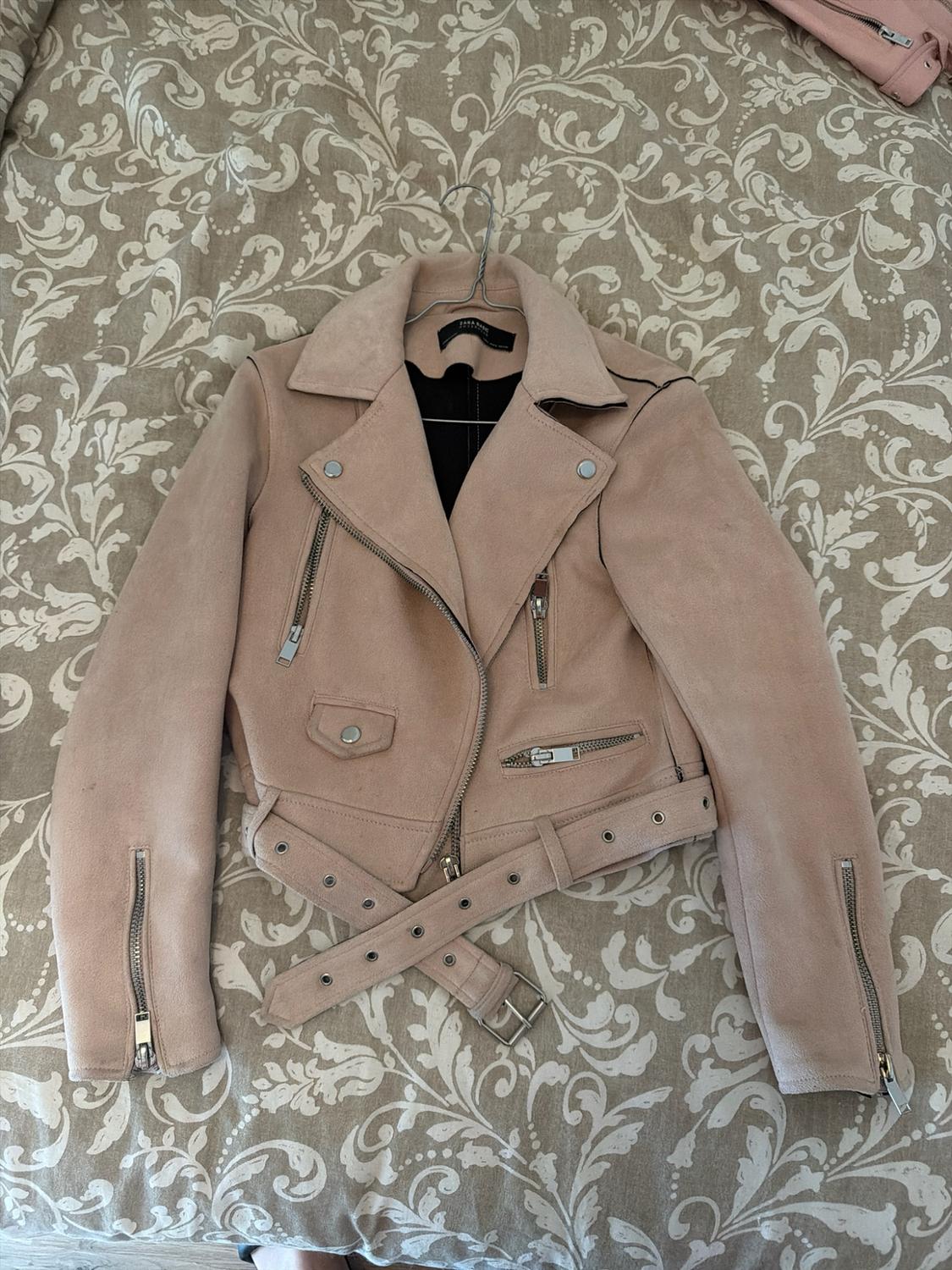 Light pink biker jacket with zips and a belt, over fabric with a floral print. The label reads ZARA BASIC.