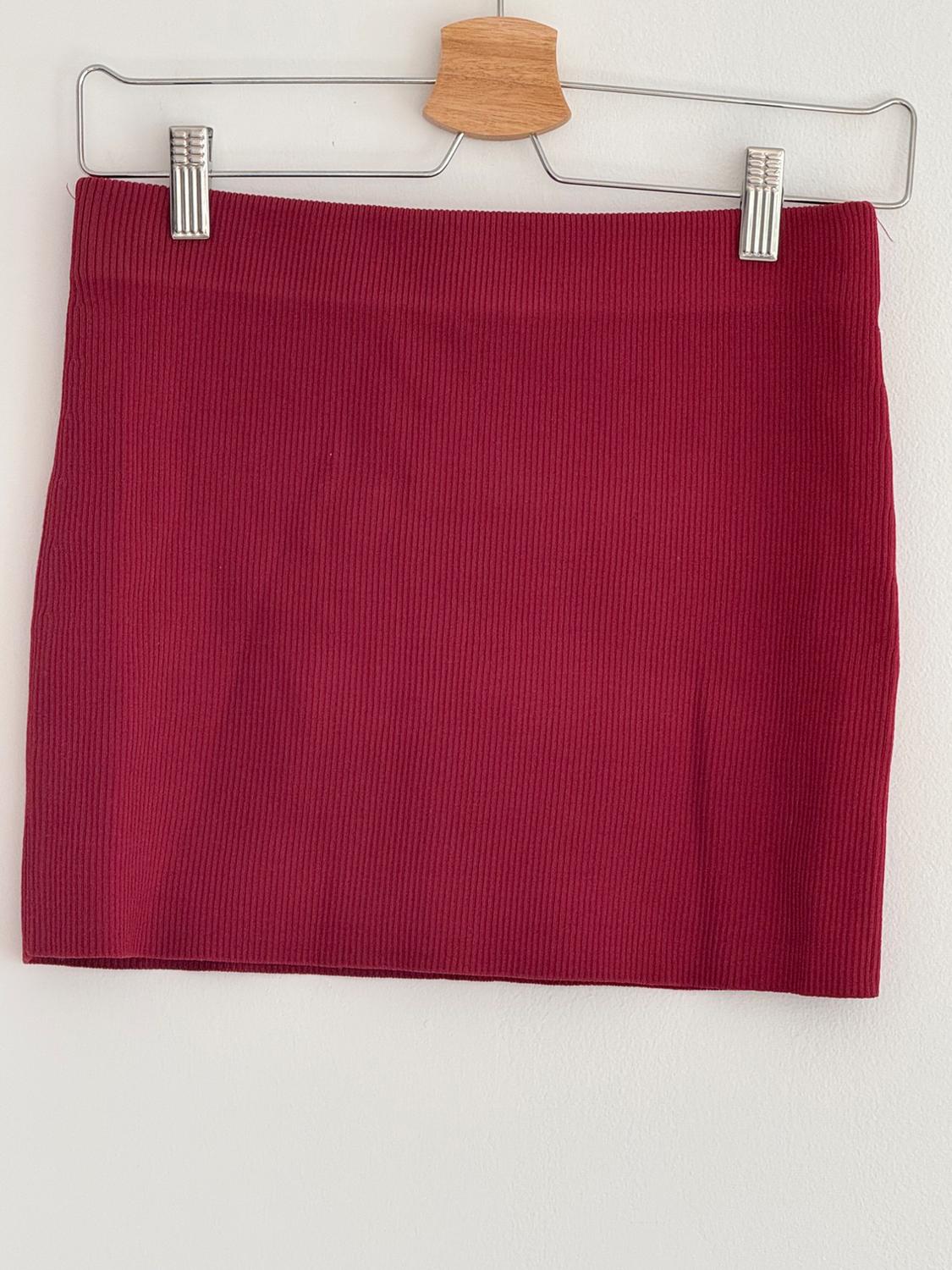 Red ribbed mini skirt hanging on a wooden hanger against a white background.