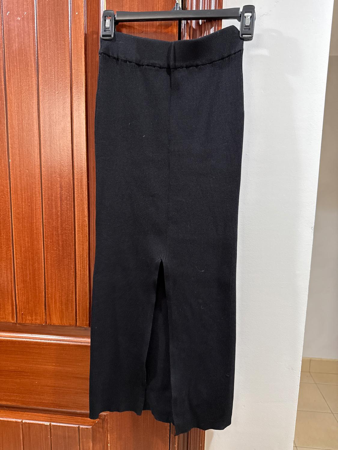 Black knit skirt hanging on a hanger over a wooden door. It has a slit at the bottom center.