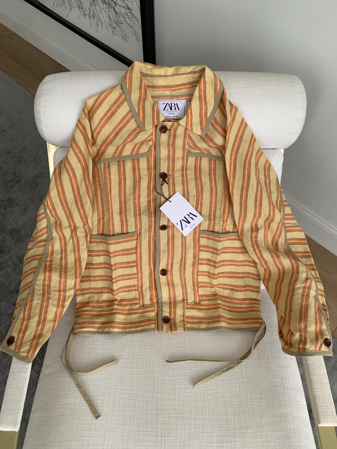 Jacket with yellow and orange stripes and buttons on a white chair. Includes labels bearing the text ZARA STUDIO.