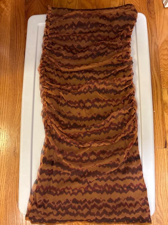 Brown fabric with a zigzag pattern in dark tones, placed on a white surface and a light wood floor.