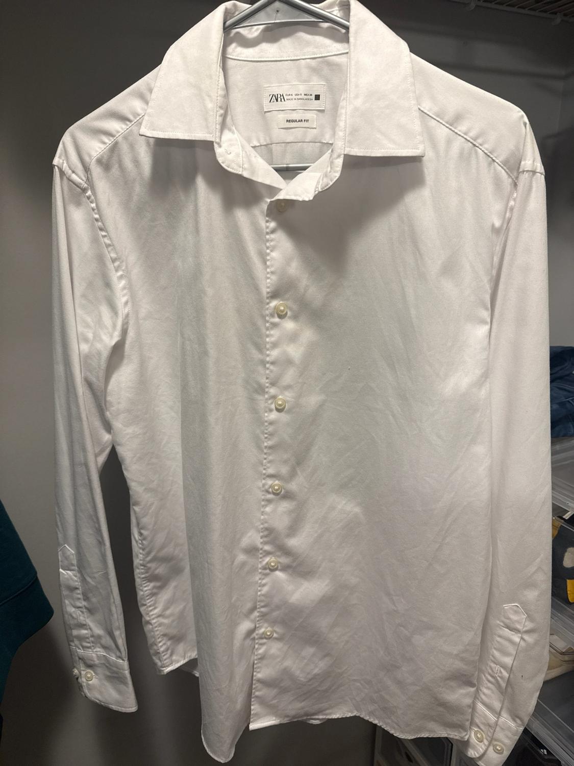 Long-sleeve white shirt from zara, regular fit cut, hanging on a hanger inside a closet.