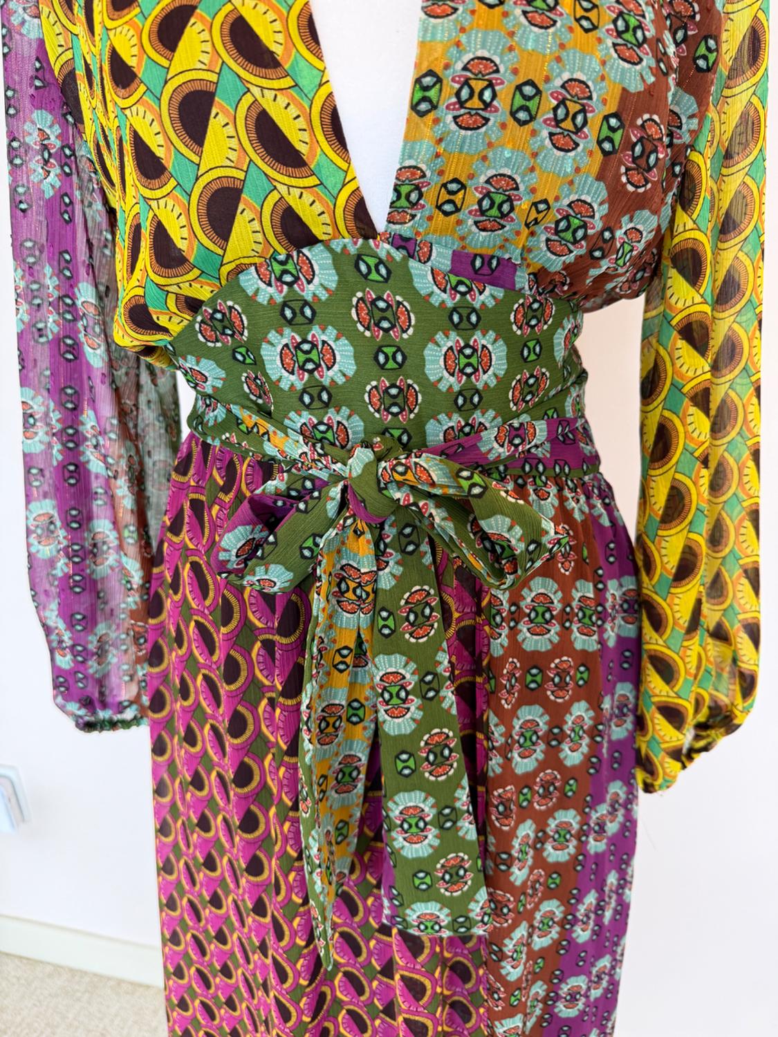 Colorful dress with geometric and floral prints in shades of green, yellow, purple, and brown, with a tie at the waist.