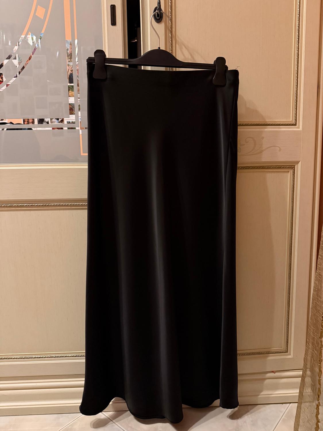 Long black skirt hanging on a black hanger over a light wooden door with decorative details. Geometric pattern background.
