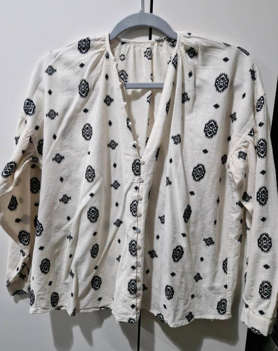 White long-sleeved blouse with a black geometric print and front buttons, hanging on a grey hanger.