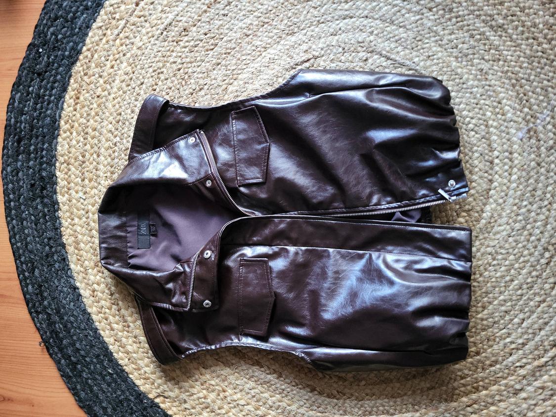 Brown faux leather waistcoat with pockets and zip, over a round jute rug in beige and black tones.