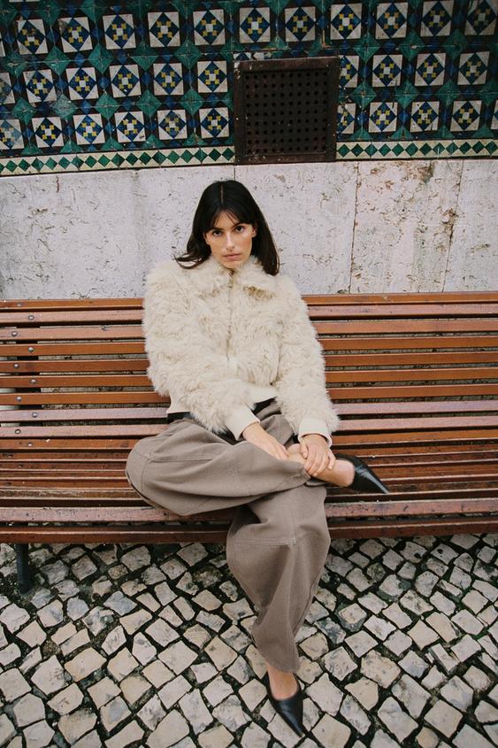 Béžová plyšová bunda na zip a hnědé široké kalhoty.