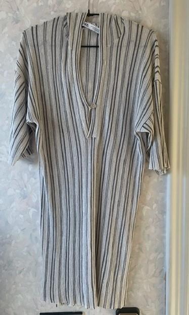 Vertical striped dress in shades of grey and beige, hanging on a hanger against a light floral wallpaper background.