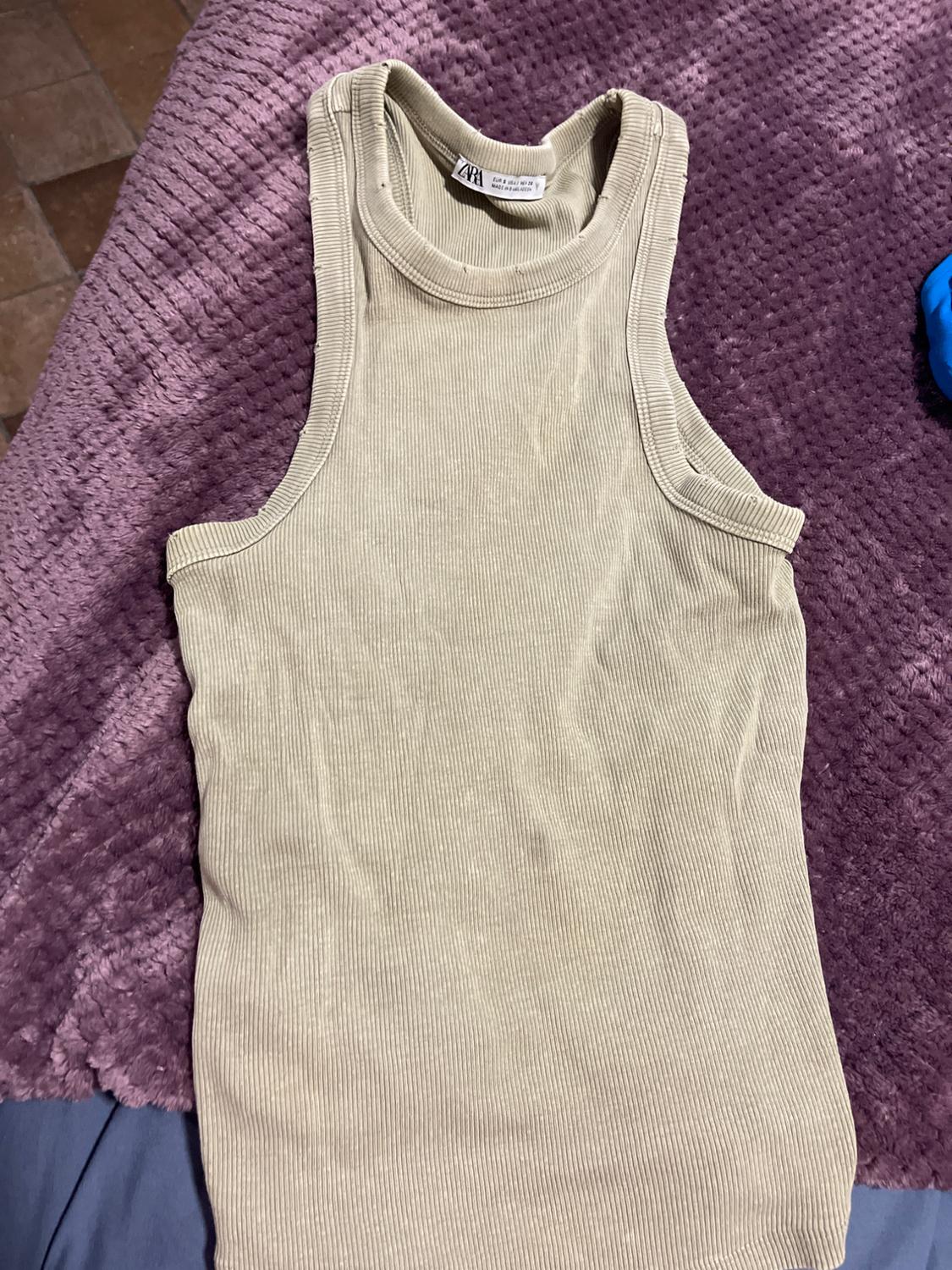 Beige sleeveless top on a textured purple blanket. Visible neck label with "ZARA" text.