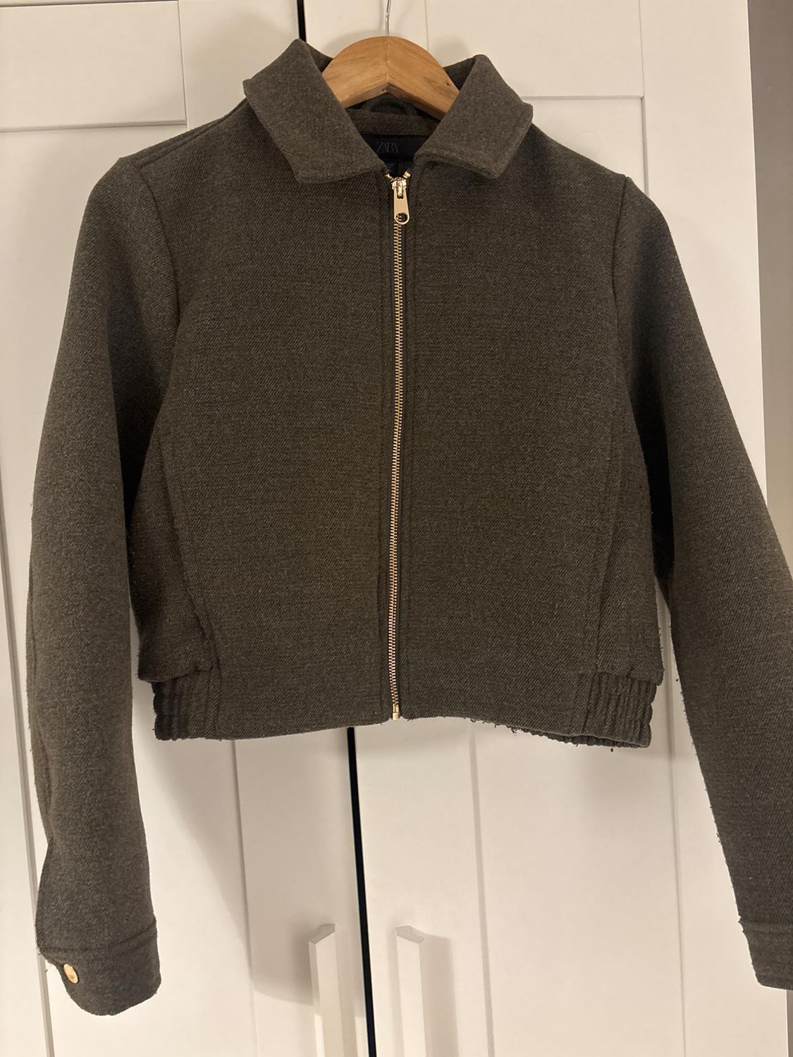 Brown jacket with a gold zip hanging on a wooden hanger in front of a white wardrobe.
