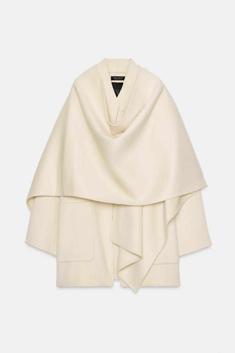 Sprednji pogled na neobdelan plašč z ovratnikom, dolgimi rokavi, našitimi žepi in snemljivo pelerino z gumbom.