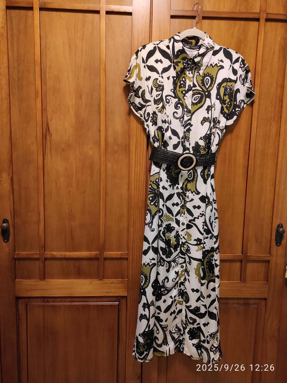 Printed dress in white, black, and green with a black belt hanging on a wooden door. Date in image: 2025/9/26 12:26.