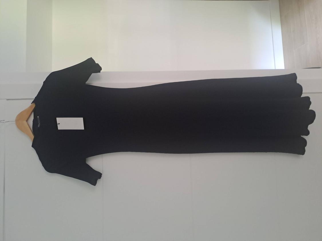 Short-sleeved long black dress with a white tag, hanging on a wooden hanger on a white door.