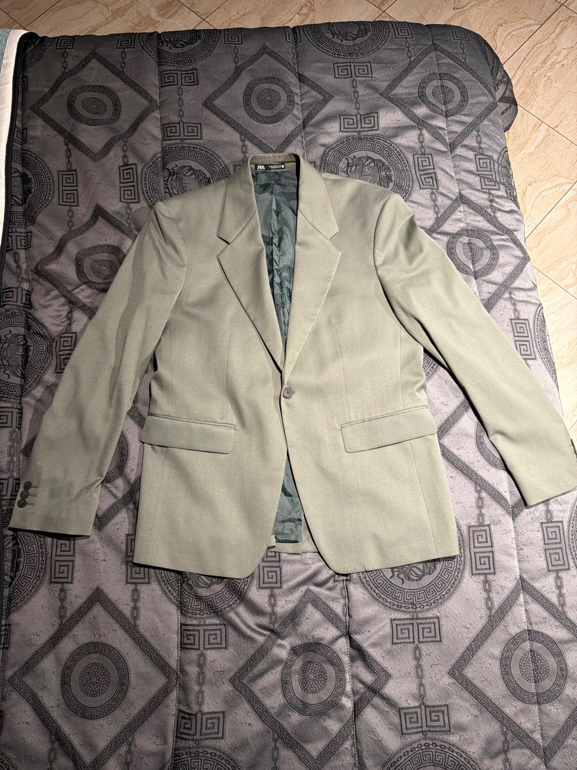 Light grey jacket on a quilt with a geometric design in shades of grey and black. The jacket has lapels and two pockets.